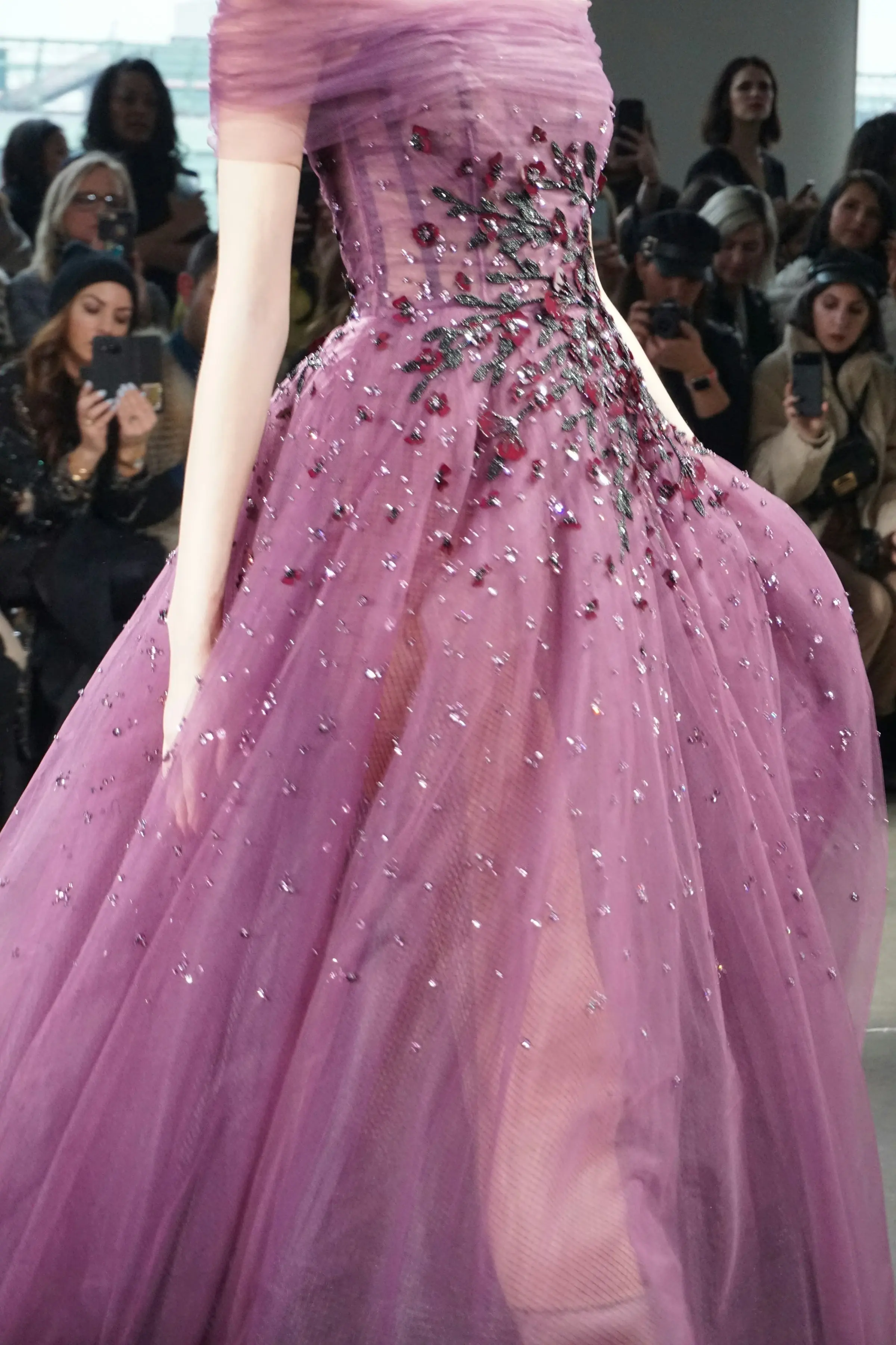 A model in a rose-pink beaded ball gown on the runway, photographers shooting from the front row